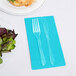 A fork and knife on a Bermuda Blue Creative Converting guest towel next to a plate of salad.