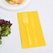 A fork and knife on a yellow napkin next to a plate of salad.