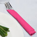 A fork and knife wrapped in a Creative Converting Hot Magenta Pink napkin.
