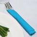 A fork and knife wrapped in a turquoise blue napkin next to a plate of green onions.