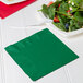 A Creative Converting emerald green luncheon napkin on a table next to a bowl of salad and a fork.
