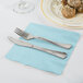 A fork and knife on a pastel blue napkin next to a plate of food.