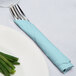 A fork and knife wrapped in a pastel blue napkin on a plate.