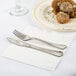 A plate of meatballs and a fork and knife on a white Creative Converting luncheon napkin.