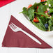 A plate of salad with a fork and a Creative Converting burgundy luncheon napkin.