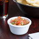 A Carlisle white melamine ramekin filled with salsa and surrounded by chips on a table.