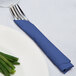 A fork and knife wrapped in a navy blue napkin next to a plate of green beans.