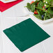 A Hunter green Creative Converting luncheon napkin next to a plate of salad with a fork.
