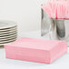 A stack of Classic Pink 1/4 Fold Luncheon Napkins on a table with pink forks and spoons.