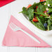 A plate of salad with strawberries and blueberries on a pink napkin with a fork.
