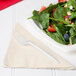 A plate of salad with strawberries and blueberries with a Creative Converting ivory luncheon napkin and a fork.