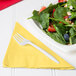 A plate of spinach salad with strawberries, nuts, and a fork with a yellow napkin on the side.
