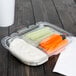 A 13 oz. clear plastic deli container with carrots, celery and cucumbers on a white table.