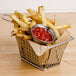 A basket of french fries with ketchup on a table with a bowl of ketchup.