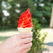 A hand holding an ice cream cone with red and white Phillips cherry shell coating.
