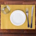 A white plate, knife, fork, and glass on a gold Hoffmaster scalloped paper placemat.