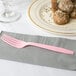 A Classic Pink plastic fork on a napkin next to a plate of food.