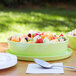 A lime melamine bowl with fruit salad on a table outdoors.