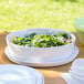 A white melamine bowl filled with salad on a table.