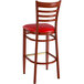 A Lancaster Table & Seating Spartan Series metal ladder back bar stool with mahogany and red vinyl seat.