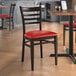 A Lancaster Table & Seating metal ladder back chair with dark walnut wood grain finish and red vinyl seat.