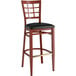 A Lancaster Table & Seating metal bar stool with a black vinyl seat on a brown surface.