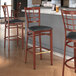 A group of Lancaster Table & Seating Spartan Series metal bar stools with black vinyl seats next to a bar counter.