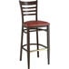 A Lancaster Table & Seating metal ladder back bar stool with dark walnut wood grain finish and burgundy vinyl seat on a table in a bar.