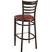 A Lancaster Table & Seating metal ladder back bar stool with a dark walnut wood grain finish and burgundy vinyl seat.