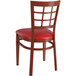 A Lancaster Table & Seating Spartan Series metal chair with mahogany wood grain finish and red vinyl seat.
