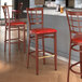 A Lancaster Table & Seating Spartan Series red bar stool with mahogany wood grain finish and a red vinyl seat.