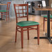 A Lancaster Table & Seating green metal chair with mahogany wood grain accents and a green vinyl cushion.