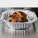 An oval foil roast pan with a cooked chicken inside.