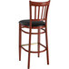 A Lancaster Table & Seating metal slat back bar stool with mahogany wood grain finish and black vinyl seat.