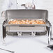 A person using a Vollrath roll top chafer cover to cook shrimp in a metal pan on a buffet table.