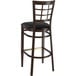 A Lancaster Table & Seating metal bar stool with a black vinyl seat and dark wood grain finish.