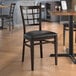 A Lancaster Table & Seating Spartan Series metal window back chair with dark walnut wood grain finish and black vinyl seat.