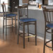 A group of three Lancaster Table & Seating Spartan Series metal slat back bar stools with navy vinyl seats next to a counter.