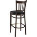 A Lancaster Table & Seating Spartan Series metal bar stool with a dark walnut wood grain finish and black vinyl seat.