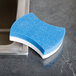 A blue and white 3M Scotch-Brite Easy Erasing Pad on a metal surface.