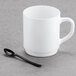 A white mug on a grey surface with a black WNA Comet tasting fork inside.