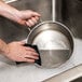 A person cleaning a stainless steel pan with a 3M Scotch-Brite blue scratchless power pad.
