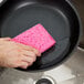 A hand using a 3M Scotch-Brite sponge to clean a pan.