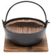 A black cast iron Thunder Group Japanese noodle bowl with wooden lid and base on a wood surface.