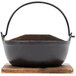 A black cast iron noodle bowl on a wooden base.