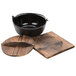 A black Thunder Group cast iron bowl with a wooden lid and base on a wooden tray.