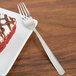 A Arcoroc stainless steel dessert fork on a plate with a piece of cake.