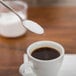 An Arcoroc stainless steel teaspoon holding sugar over a cup of coffee.