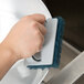 A hand using a 3M Twist-Lok Pad Holder with a blue sponge to clean a stainless steel sink.