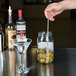 A hand using an American Metalcraft stainless steel bar ejector fork to pour olives into a glass of clear liquid.